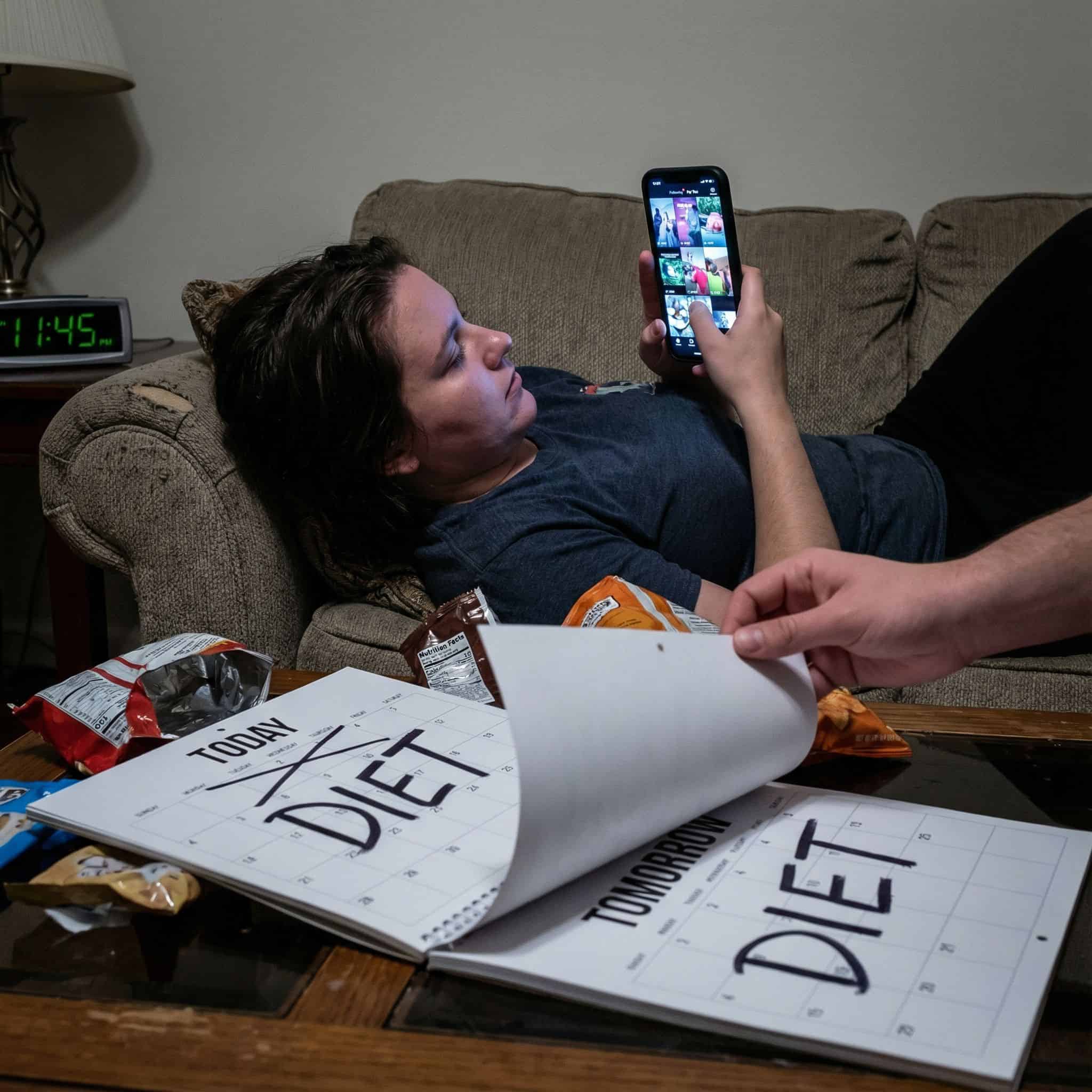 한 손으로 스마트폰을 들고 짧은 영상을 계속 넘기며, 다른 손으로는 다이어트라고 적힌 달력 페이지를 내일